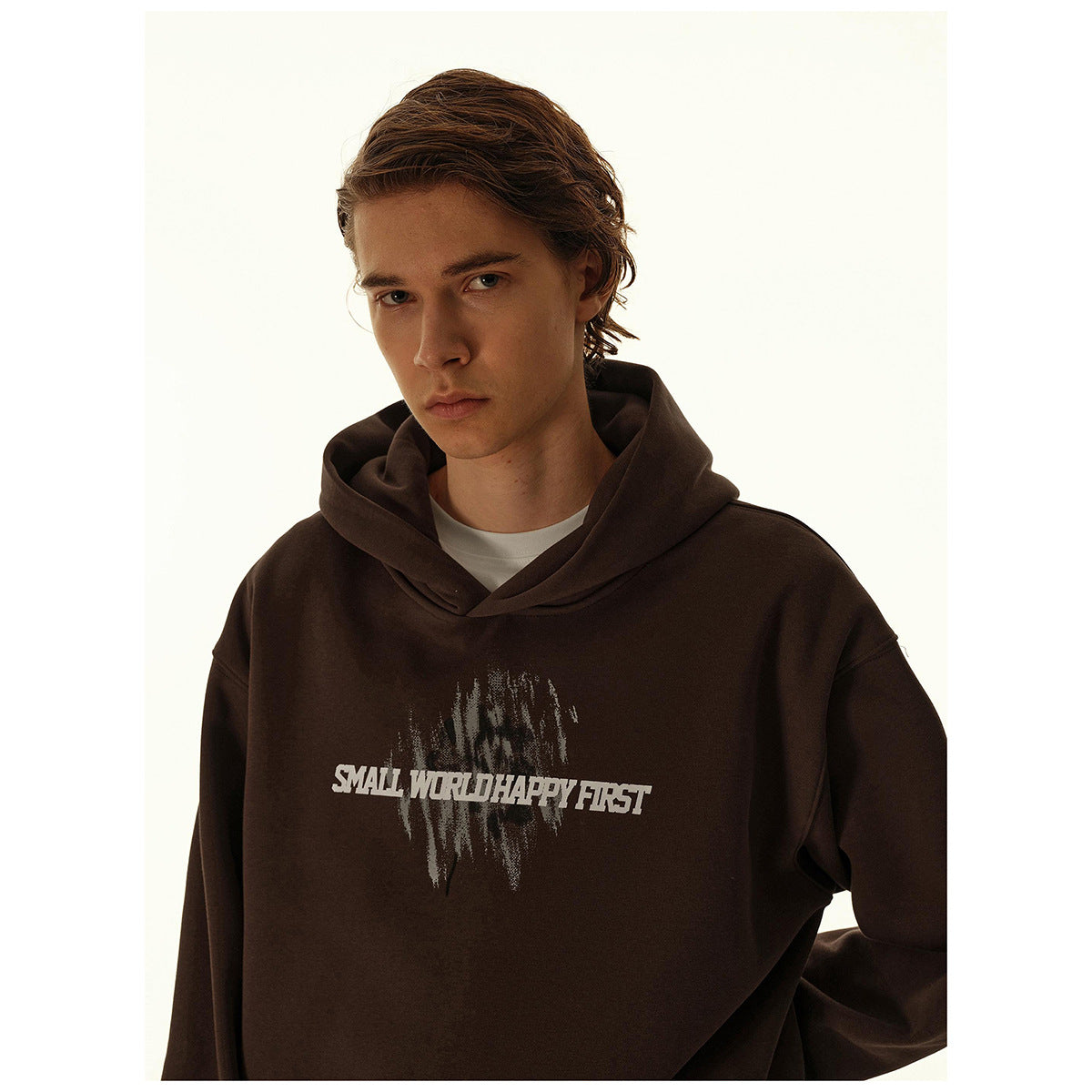 Close-up of a model wearing a dark brown hoodie with a distressed graphic and white text across the chest.