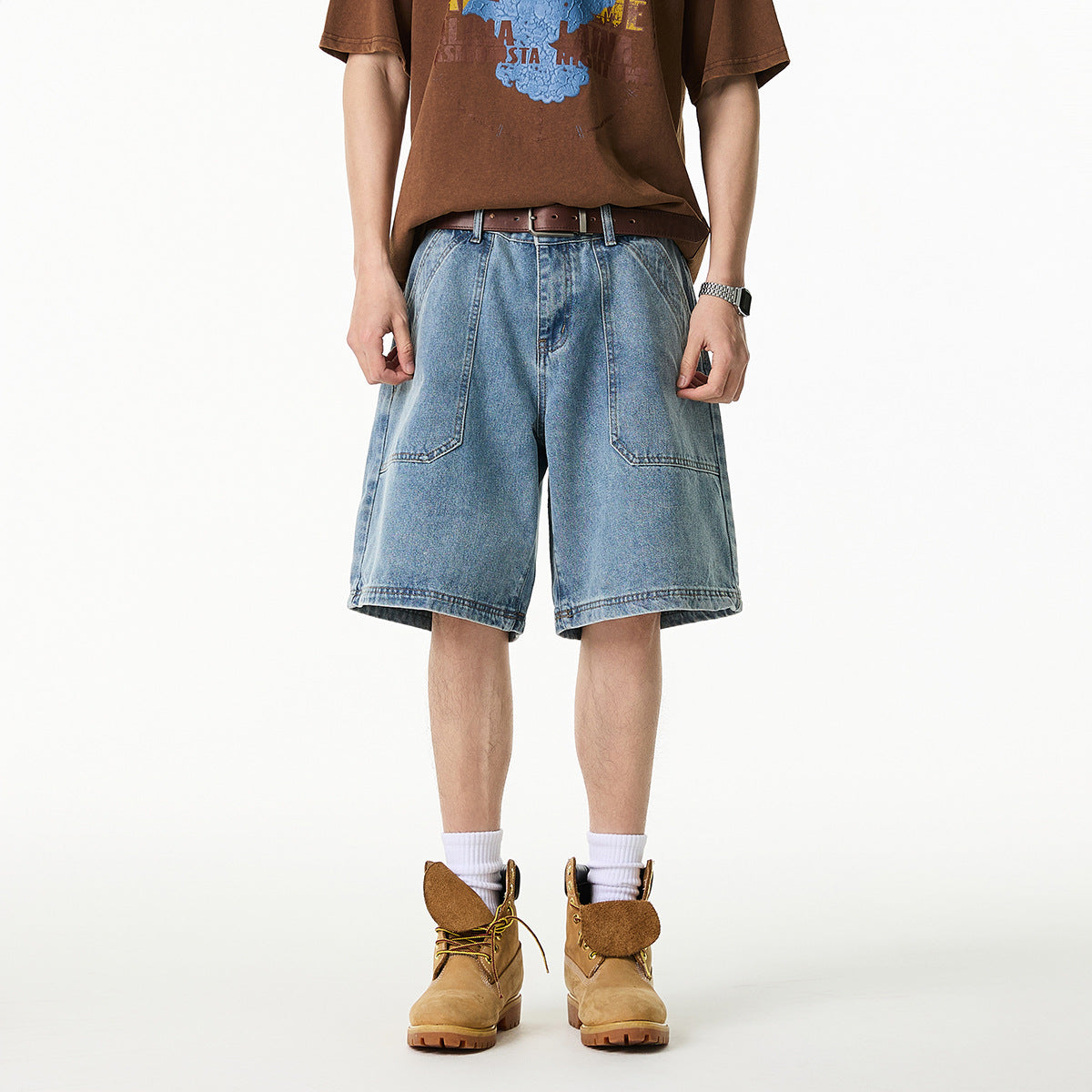 Front view of a person wearing wide light-wash denim shorts with large front pockets and a brown graphic T-shirt.