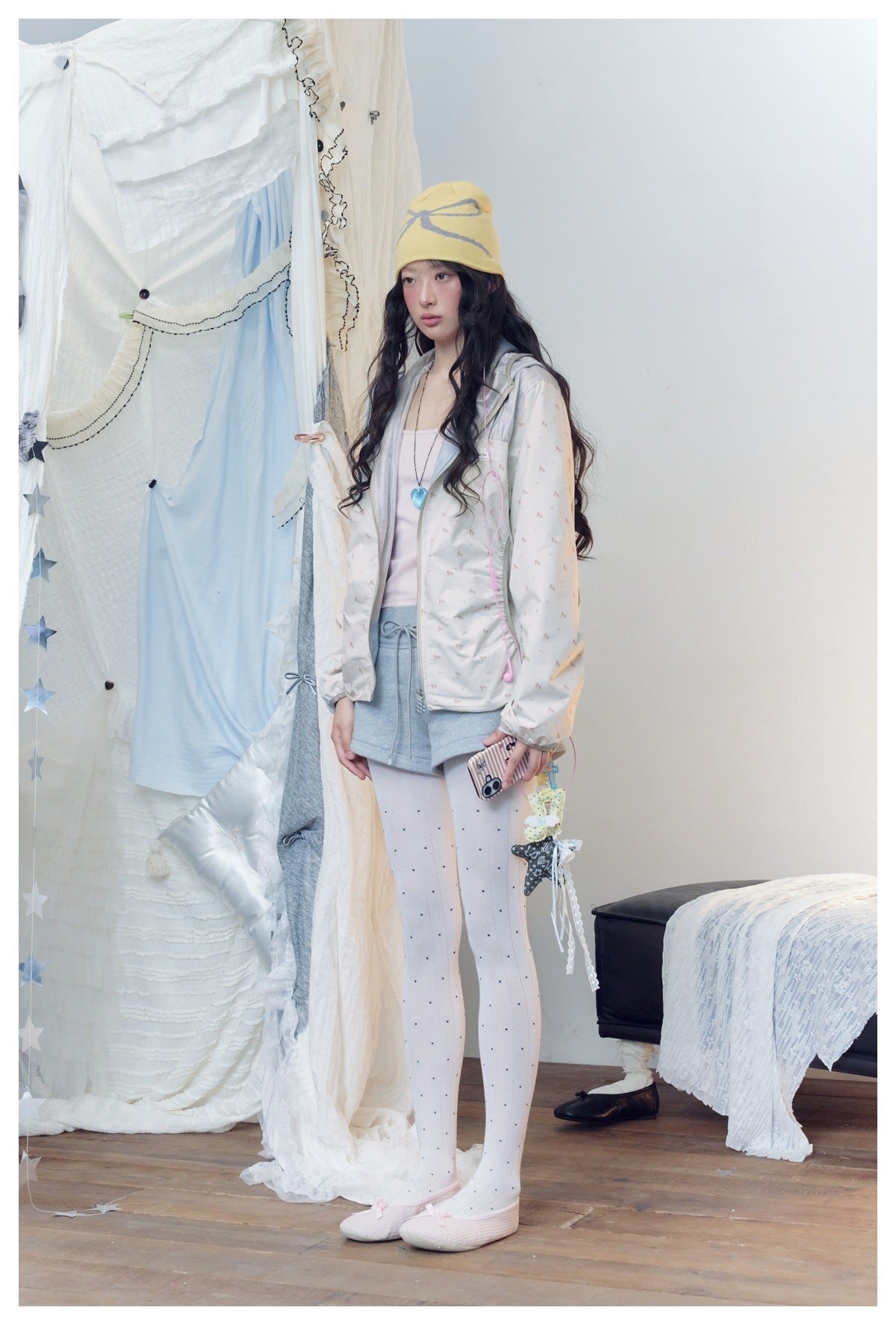 Model in a floral off-white hooded zip jacket, angled three-quarter view with gray shorts and yellow beanie