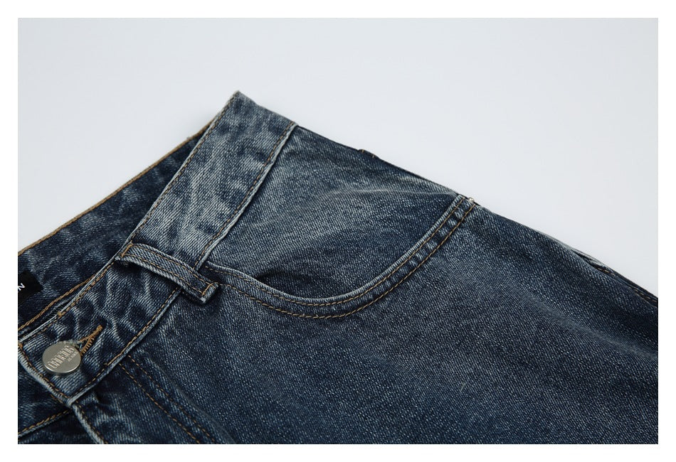 Close-up of dark blue jeans showing the waistband, belt loop, metal button and curved front pocket.