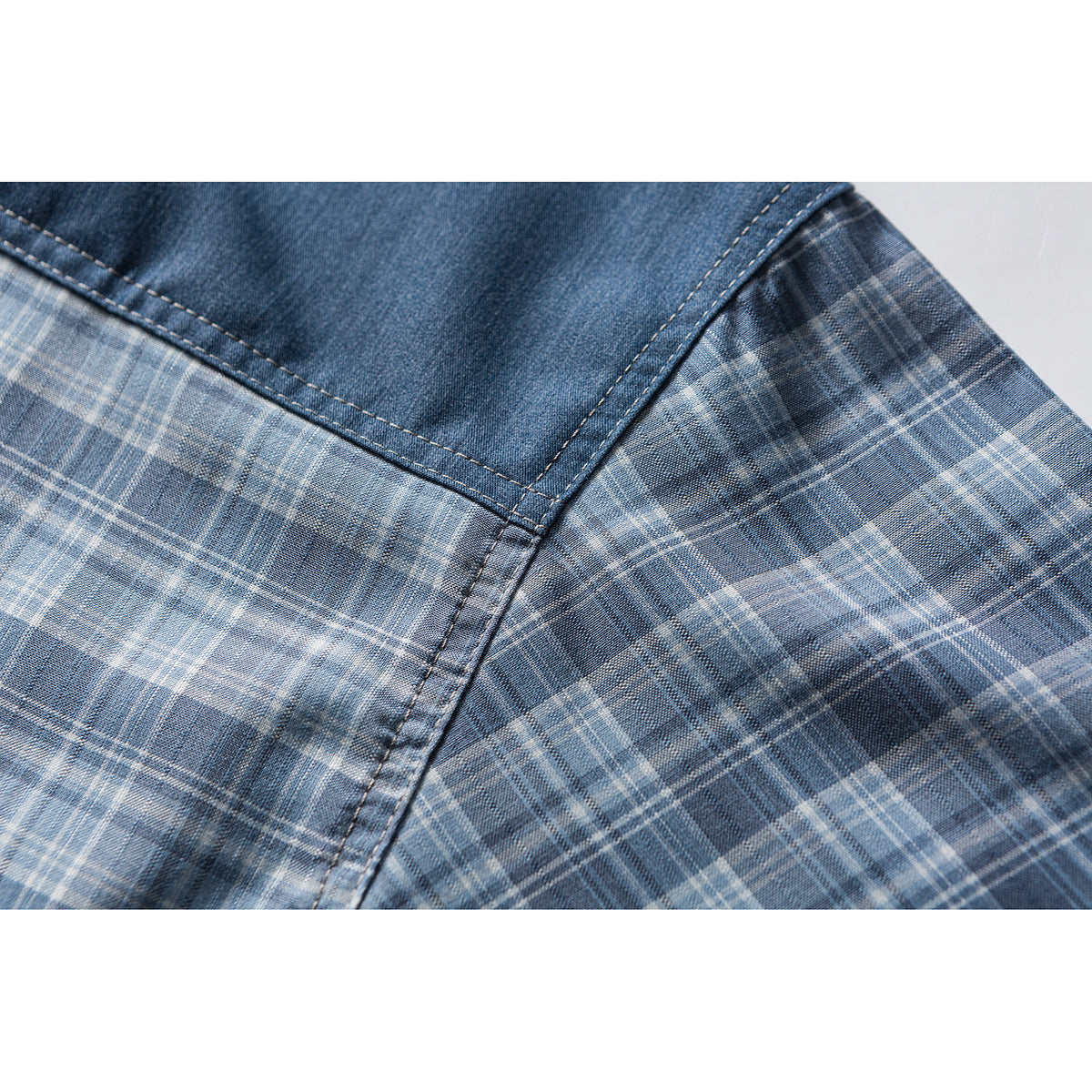 Close-up of blue plaid shirt fabric with a solid denim-look panel and visible stitching.