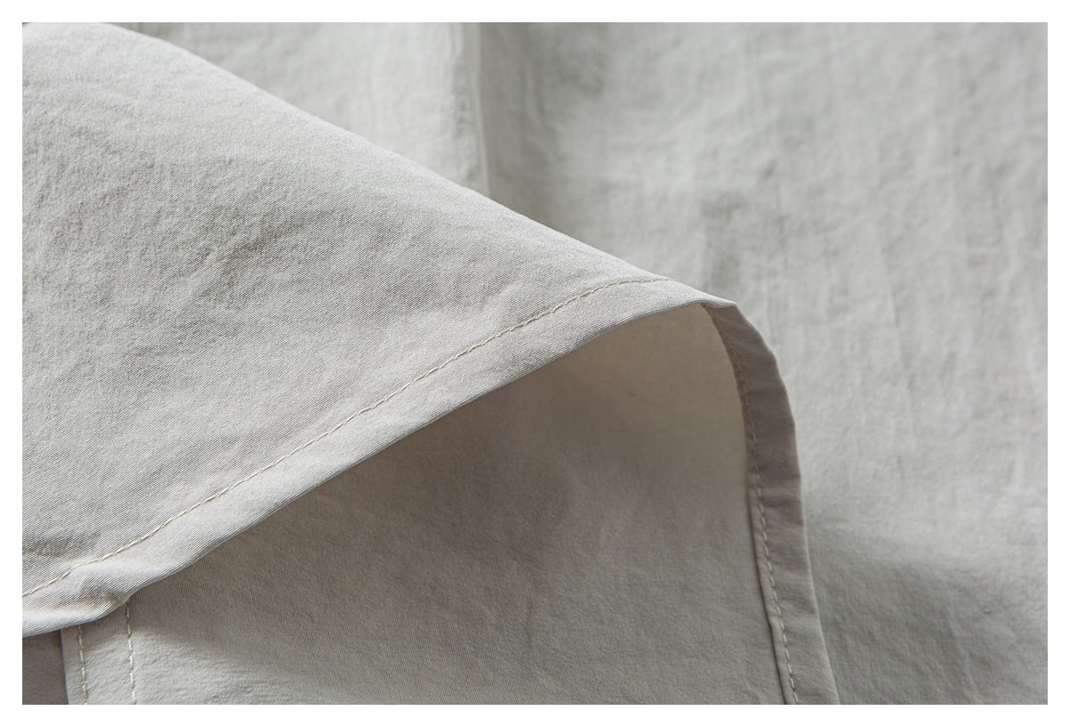 Close-up of light gray-beige fabric with a folded edge and visible stitching.