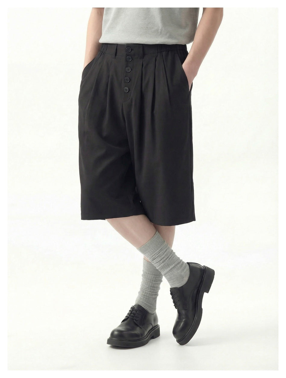Model wearing black knee-length wide-leg shorts with front buttons and pleats, shown in a relaxed crossed-leg pose.