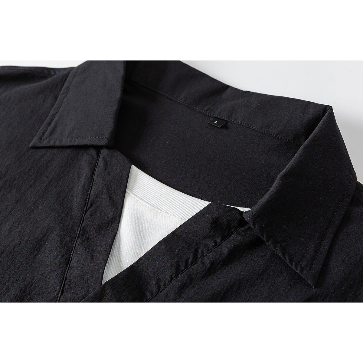 Close-up of a black collared garment with a V-shaped opening, white inner layer, and small L size tab.