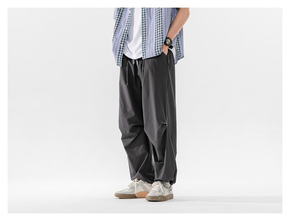 Side view of a cropped model wearing relaxed charcoal-gray trousers with a drawstring waist and gathered hems.