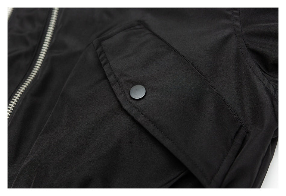 Close-up of a black jacket's angled flap pocket with a dark snap button.
