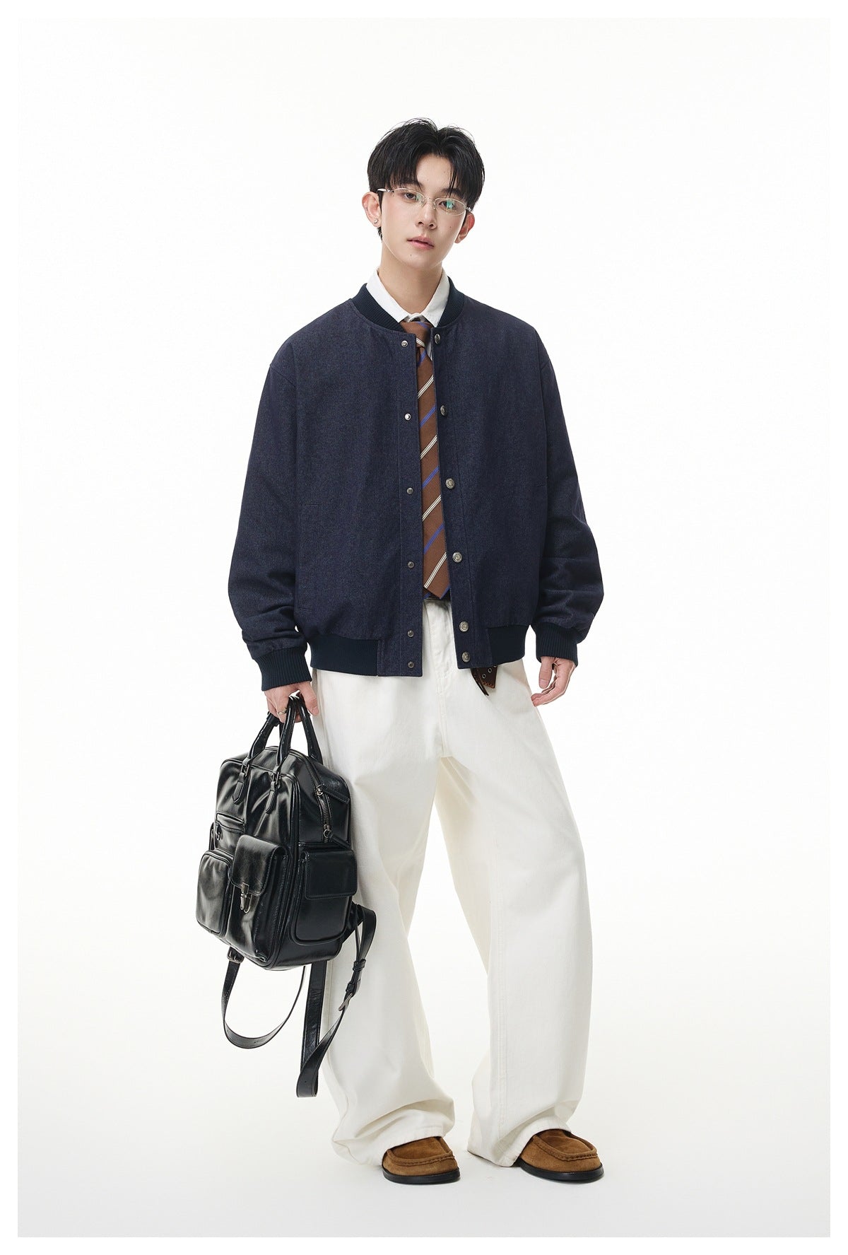 Full-length model wearing a dark navy snap-front jacket with ribbed trim, white trousers, and brown shoes.