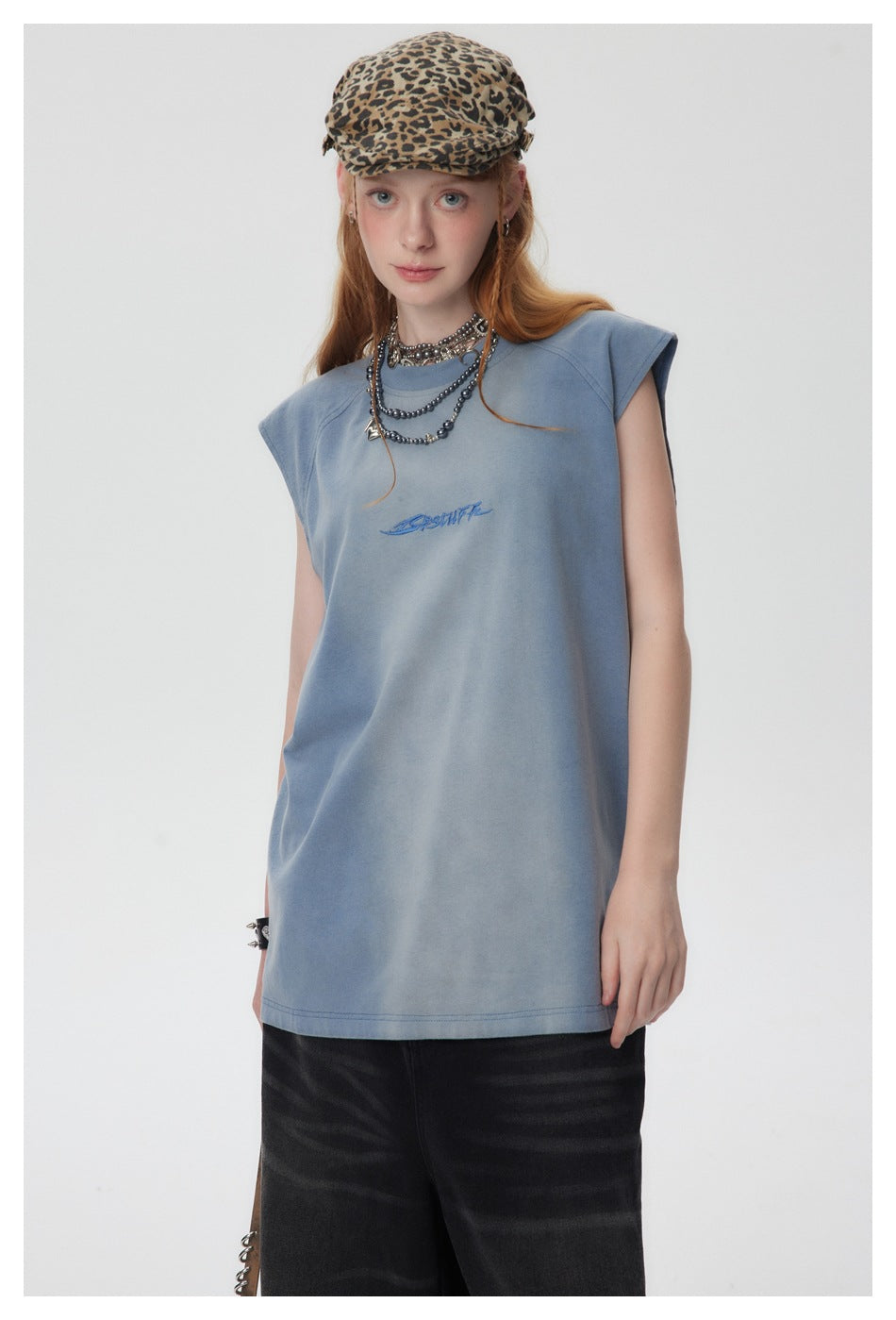 Full-length front view of a model wearing a slate-blue sleeveless top with blue chest embroidery and black trousers.