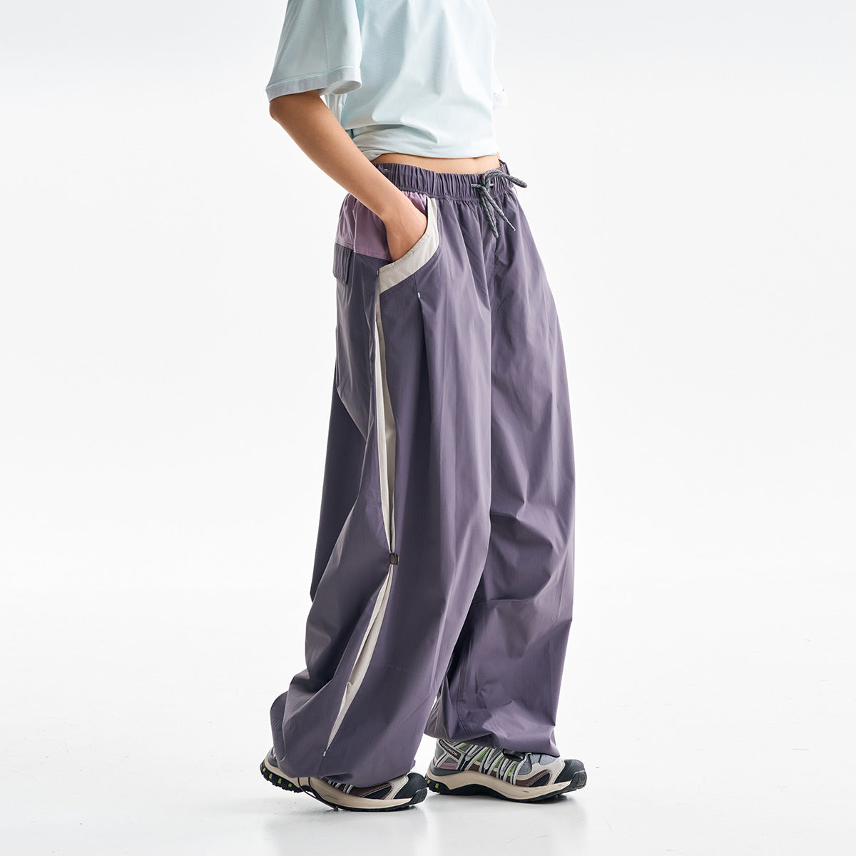 Side view of a person wearing loose purple drawstring pants with light side panels and zip details.