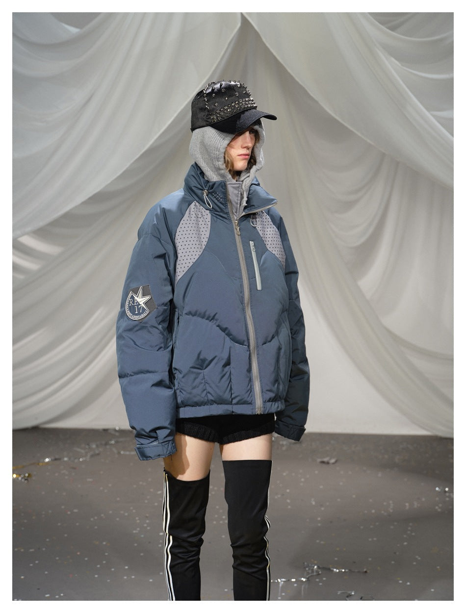 Angled view of a model wearing a blue-gray puffer jacket with dotted panels, chest zipper pocket, and sleeve patch.