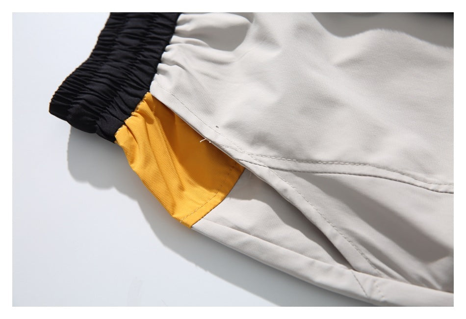 Close-up of a light gray shorts seam beside the black waistband and mustard-yellow side panel.