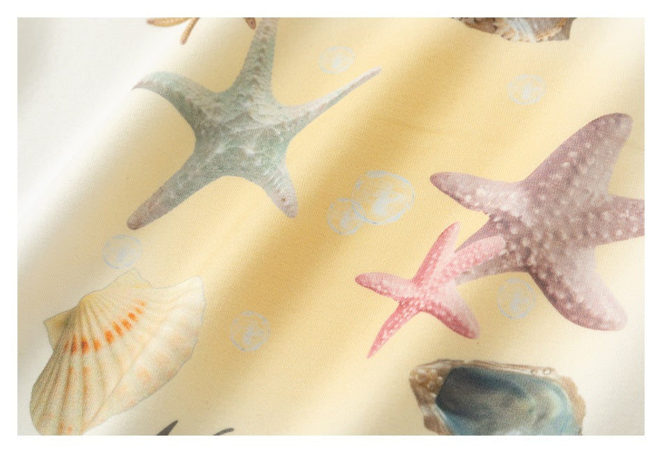 Close-up of cream fabric printed with pastel starfish, seashells, and small bubbles.