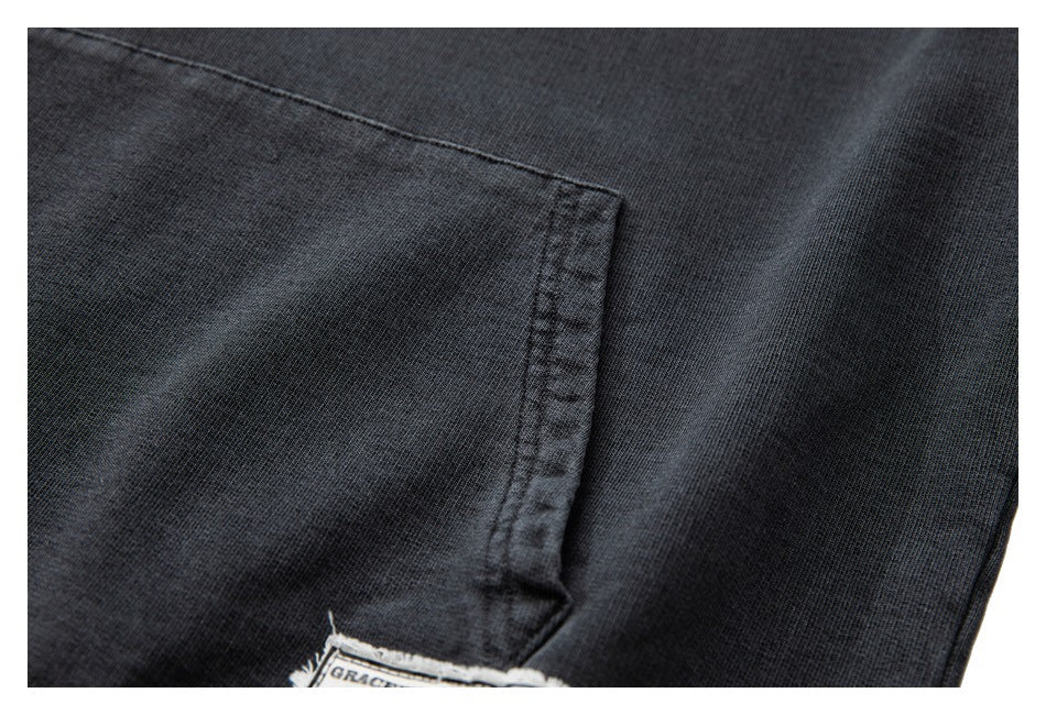 Close-up of a charcoal hoodie pocket seam and fabric, with part of a sewn label visible at the bottom.
