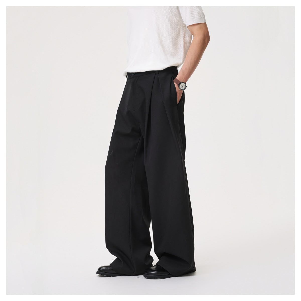 Model wearing black pleated wide-leg trousers with white top and black shoes, three-quarter view