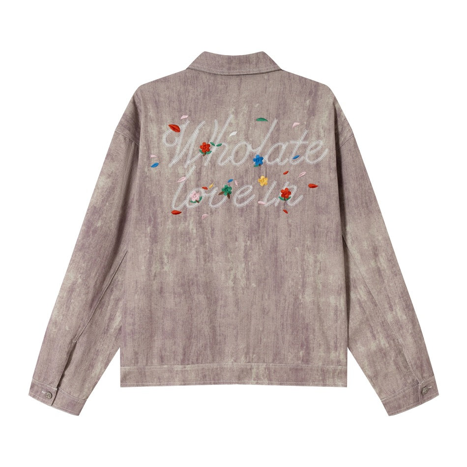 Back view of a mauve washed jacket with large white embroidered lettering and colorful flowers across the upper back.