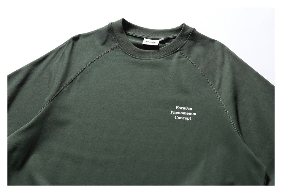 Close-up of the dark green raglan T-shirt's neckline, stitching, and small white English chest print.