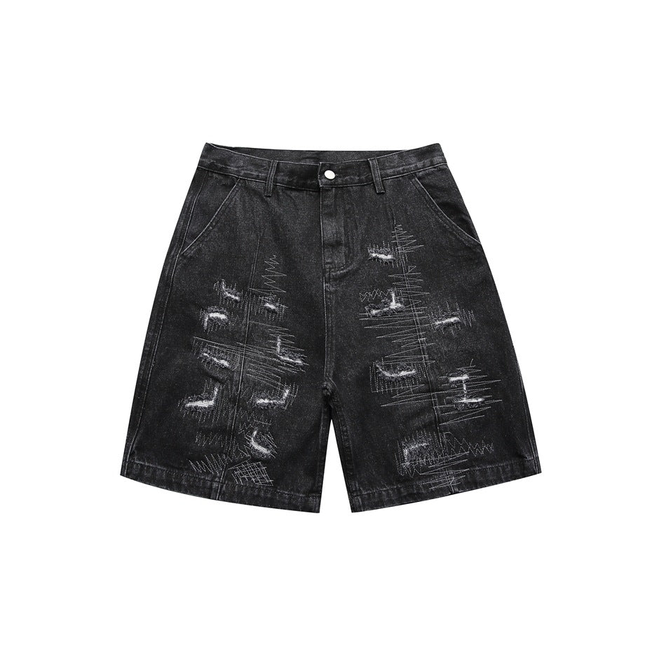 Washed black denim shorts front with white embroidery and distressed patches, flat lay on white