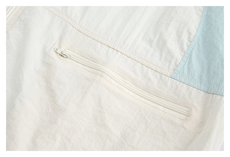 Close-up of a horizontal white zip pocket on a cream jacket panel beside pale blue trim.