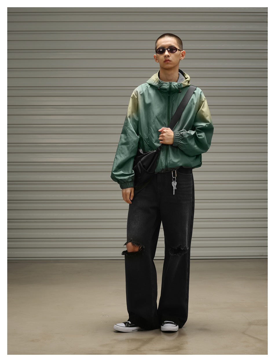 Front view of a model wearing a sage green hooded zip jacket with olive accents and black ripped jeans.