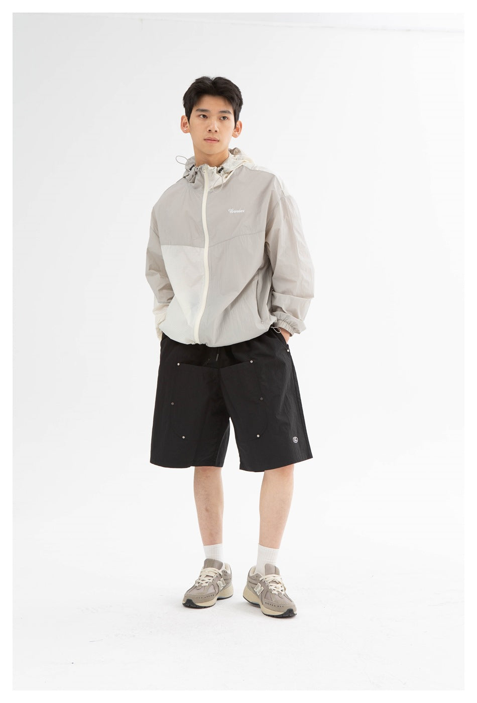 Model wearing a light gray and white hooded jacket with black utility shorts, shown full length from the front.
