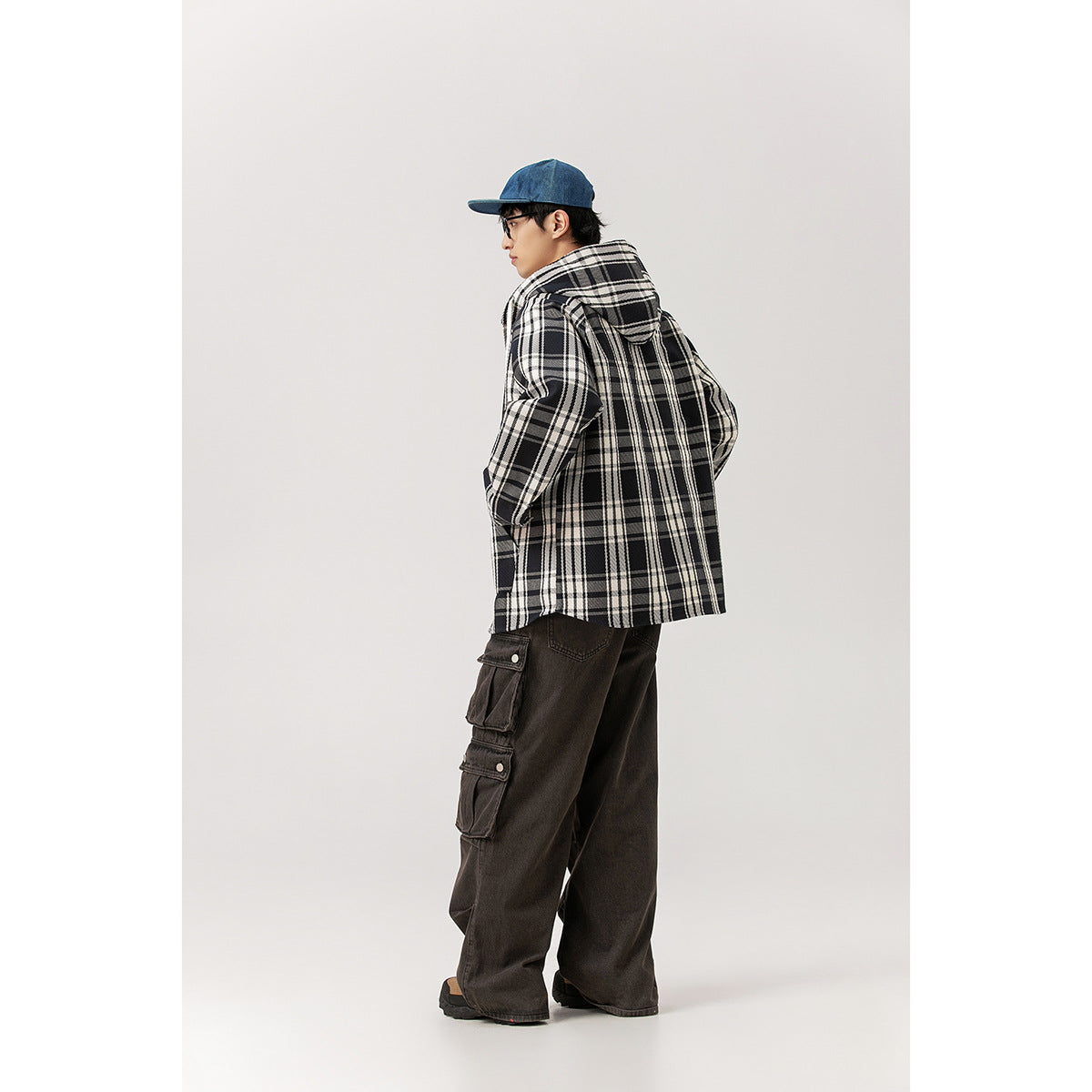 Rear view of a model wearing a black-and-white plaid hooded jacket and dark cargo pants.