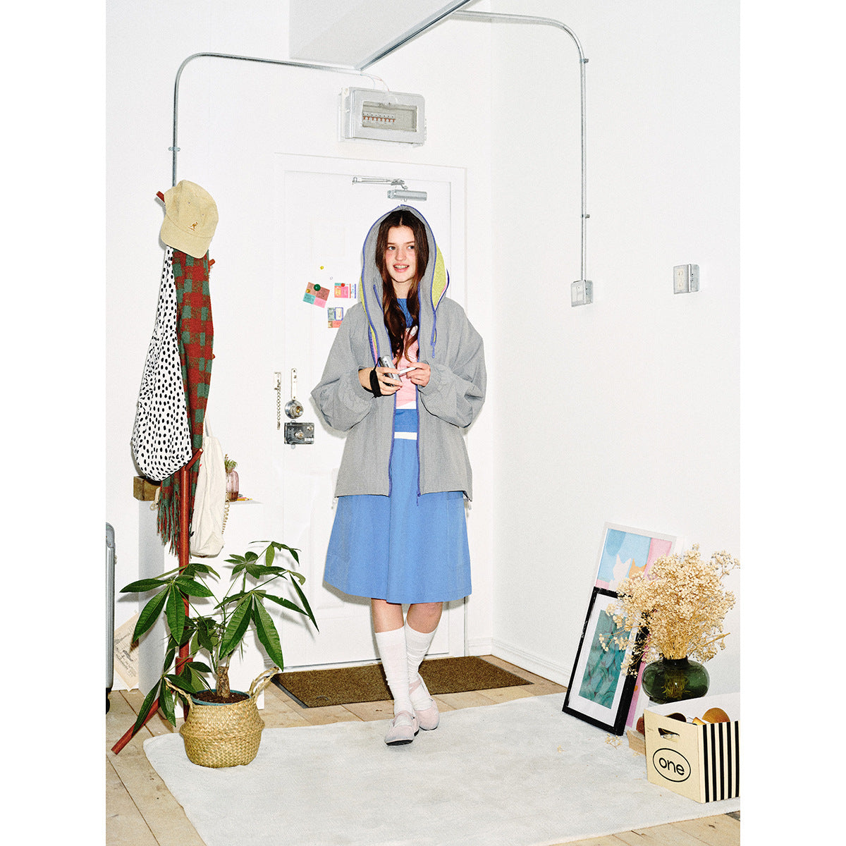 Full-length view of a model in a gray hooded jacket with colorful lining over a blue dress.