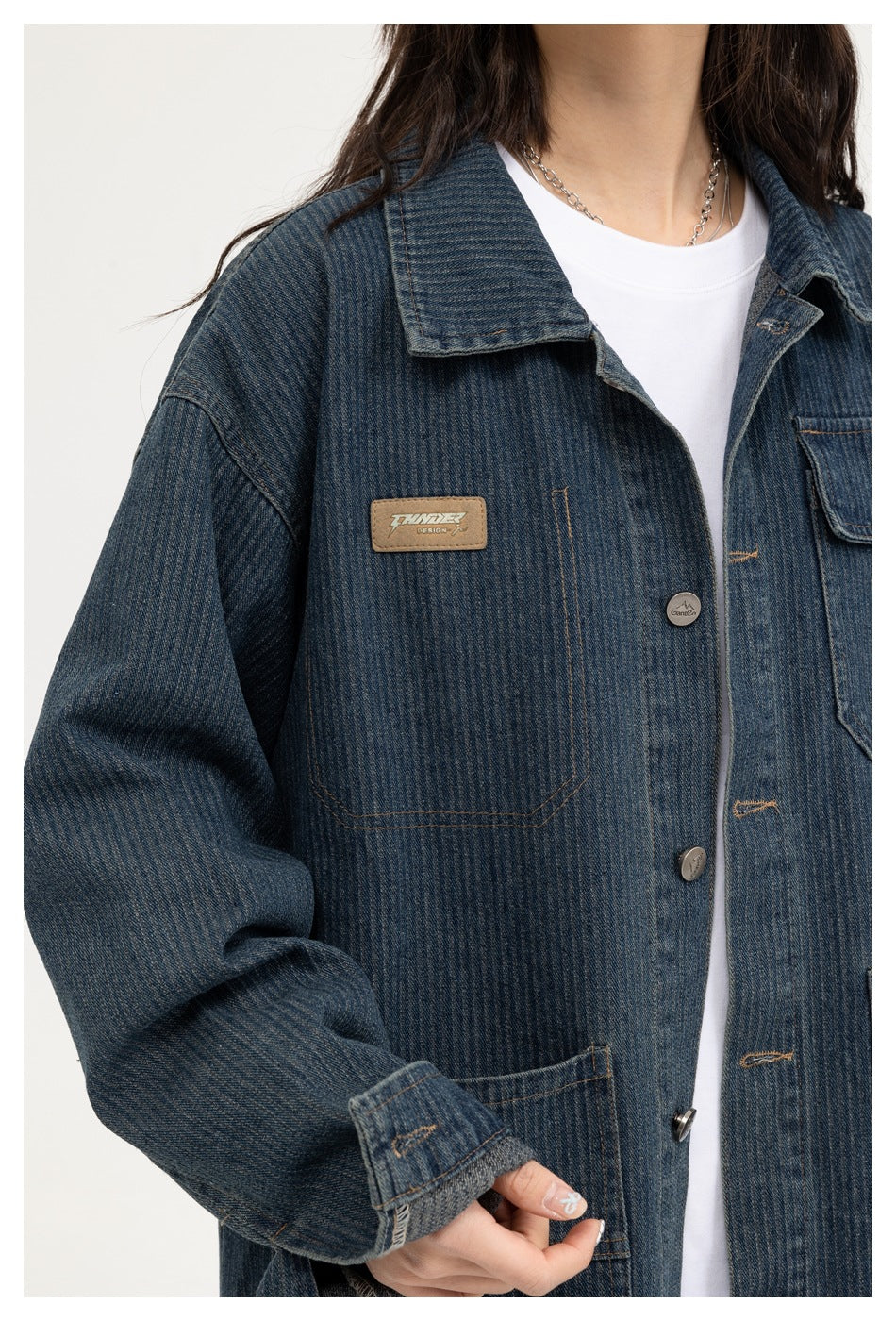 Close view of a person wearing a dark blue denim chore jacket with a collar, metal buttons and multiple pockets.