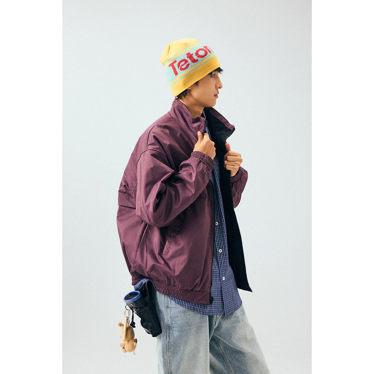 Model wearing an open plum windbreaker with black lining, blue checked shirt, and light jeans.