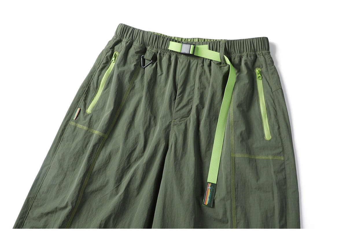 Cropped front view of olive green check-pattern pants with lime zip pockets, an elastic waist and a bright green belt.