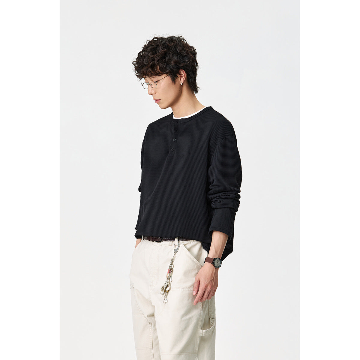 Model wearing a black long-sleeve ribbed henley shirt with a short button placket, shown from a three-quarter angle.