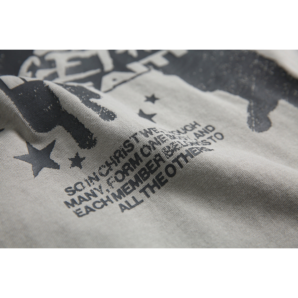 Close-up of the gray T-shirt’s printed figures, stars, and English text on folded fabric.