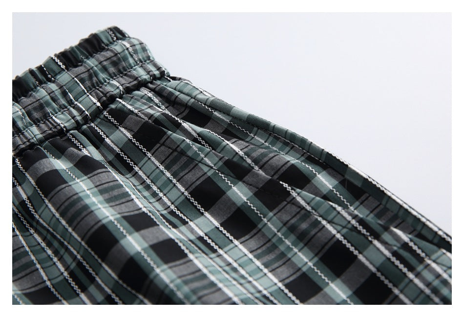 Close-up of a gathered elastic waistband on black, gray, and muted green plaid trousers.