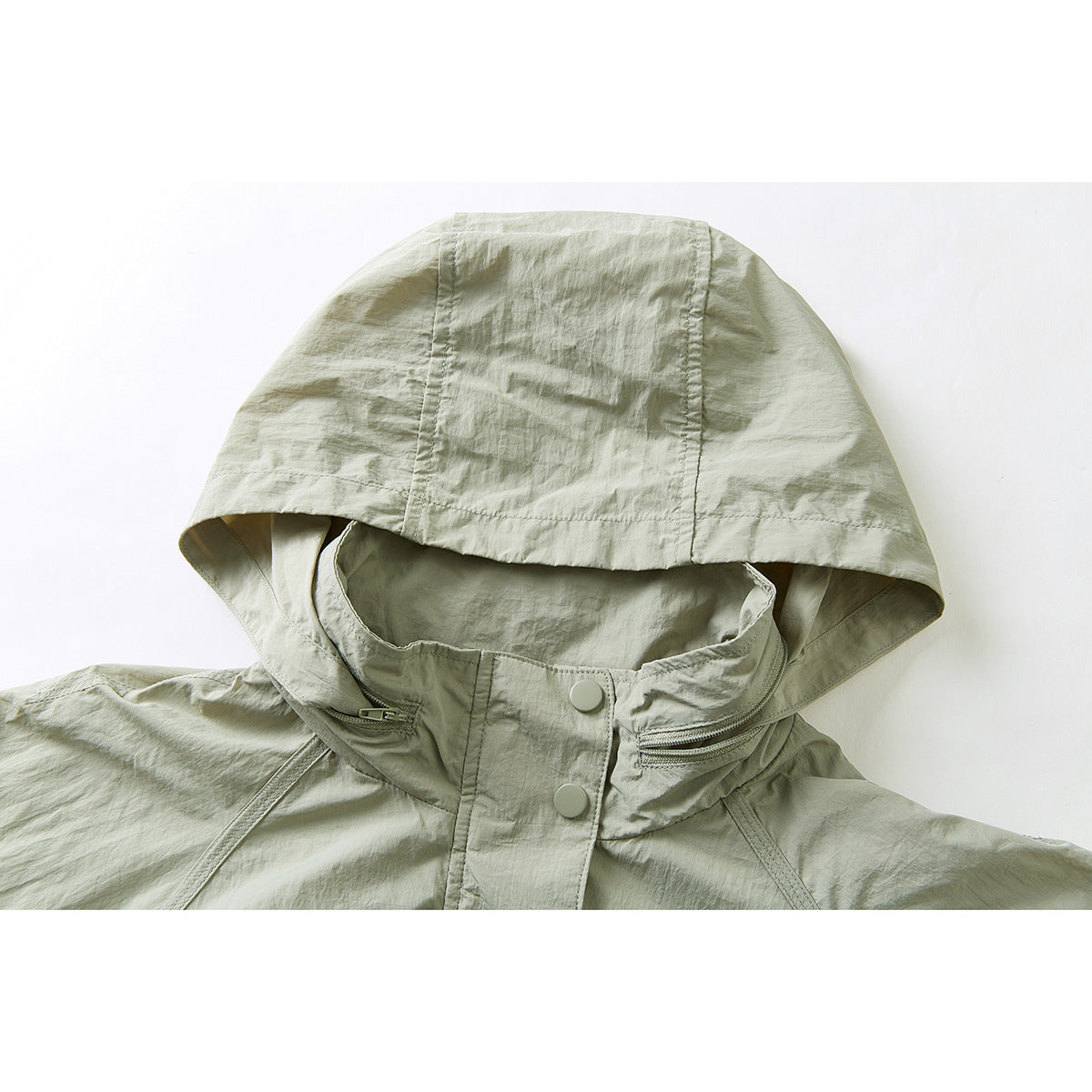 Close-up of a pale sage hooded jacket showing the oversized hood, zippered collar pockets, and snap-button placket.