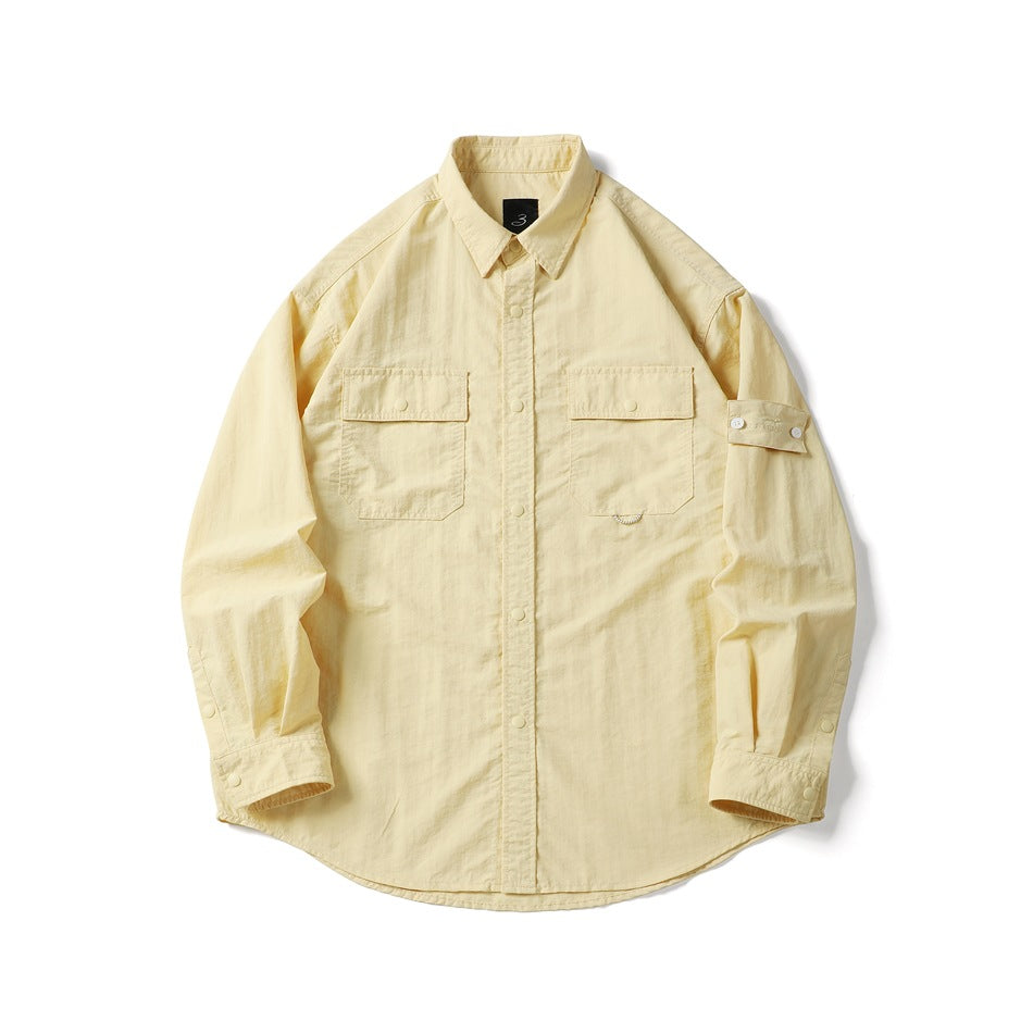 Light yellow long-sleeve utility shirt with two flap chest pockets, snap placket and sleeve strap, flat lay front view