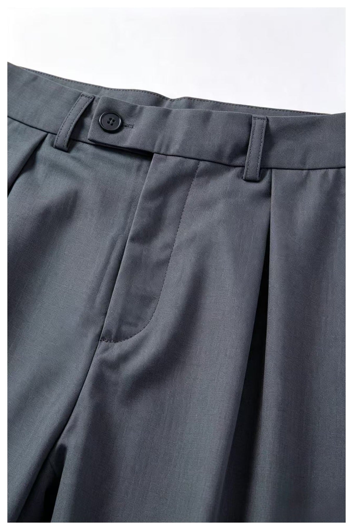 Close-up of charcoal-gray trousers showing the buttoned waistband, belt loops, fly, and front pleats.