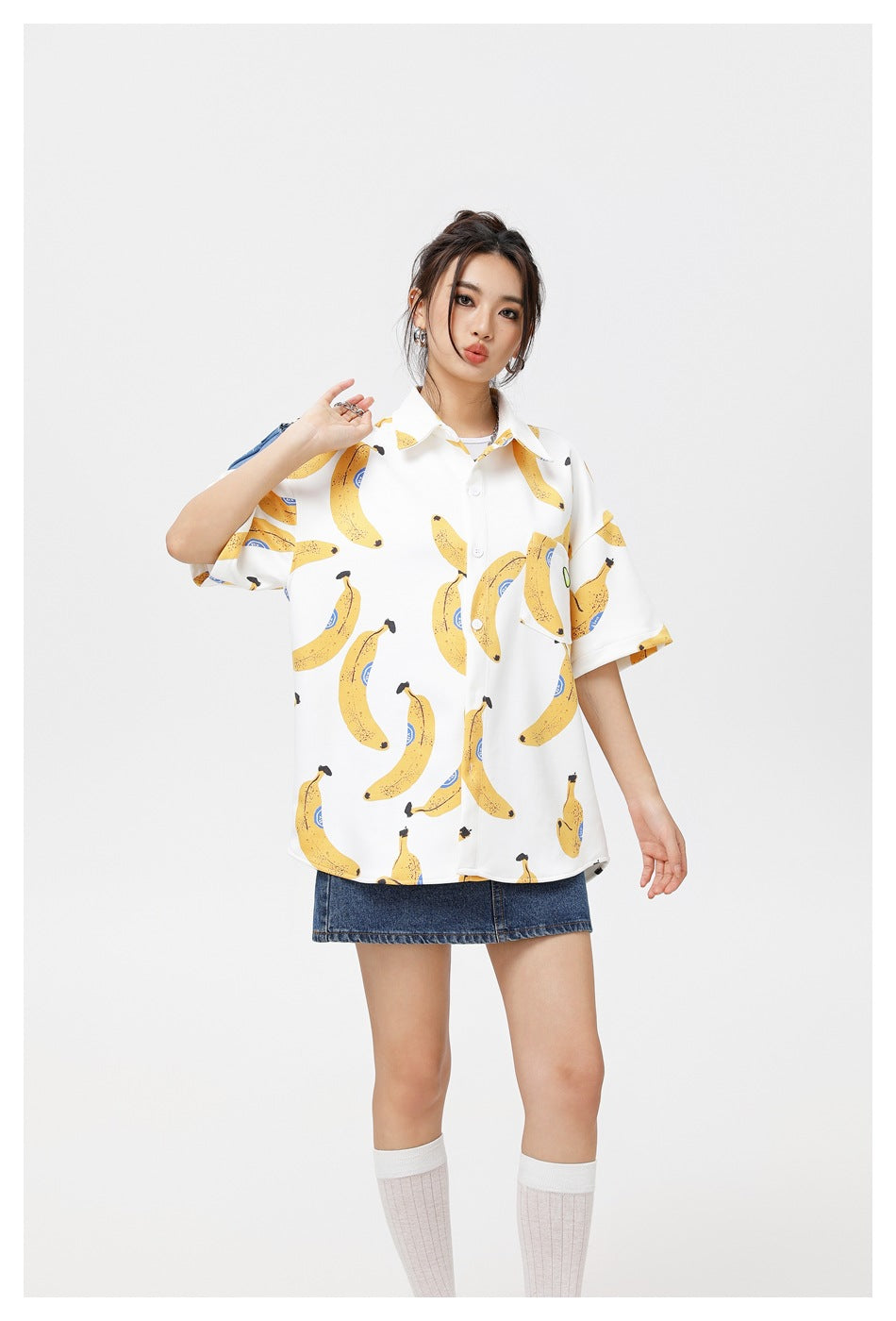Model posing in an oversized white shirt with a yellow banana print and a blue denim skirt.