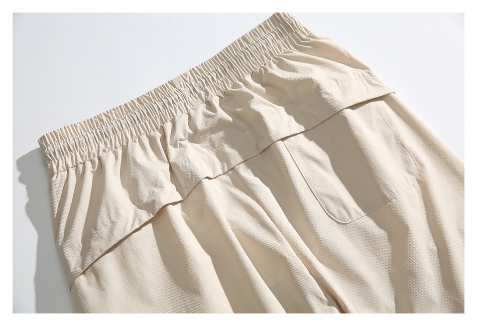 Flat lay of cream pants showing the gathered waistband, front panels and a patch pocket.