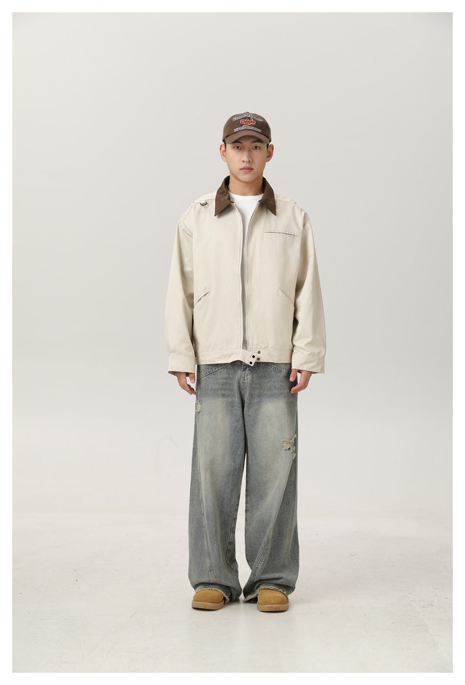 Model wearing beige zip jacket with brown collar, white tee, faded wide-leg jeans and brown cap, front view