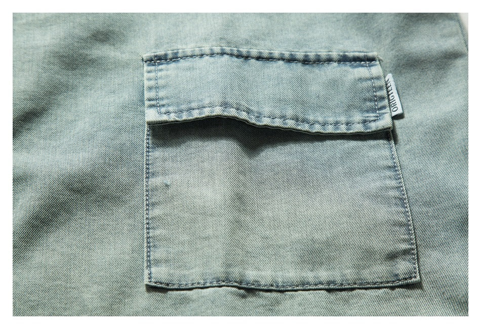 Close-up of a flap chest pocket on light blue denim, with a small sewn-in side label.
