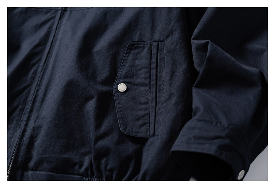 Close-up of a dark navy jacket showing a flap chest pocket with a silver snap and part of the zipper.