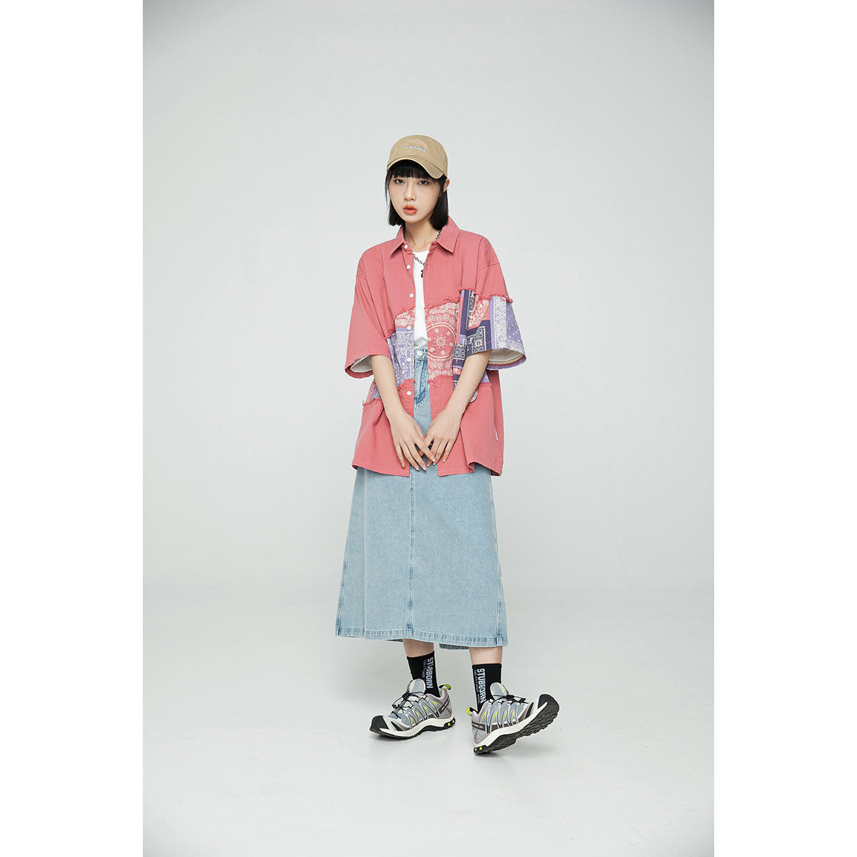 Model wearing a coral-pink oversized shirt with a multicolor bandana-print panel and a light denim midi skirt.