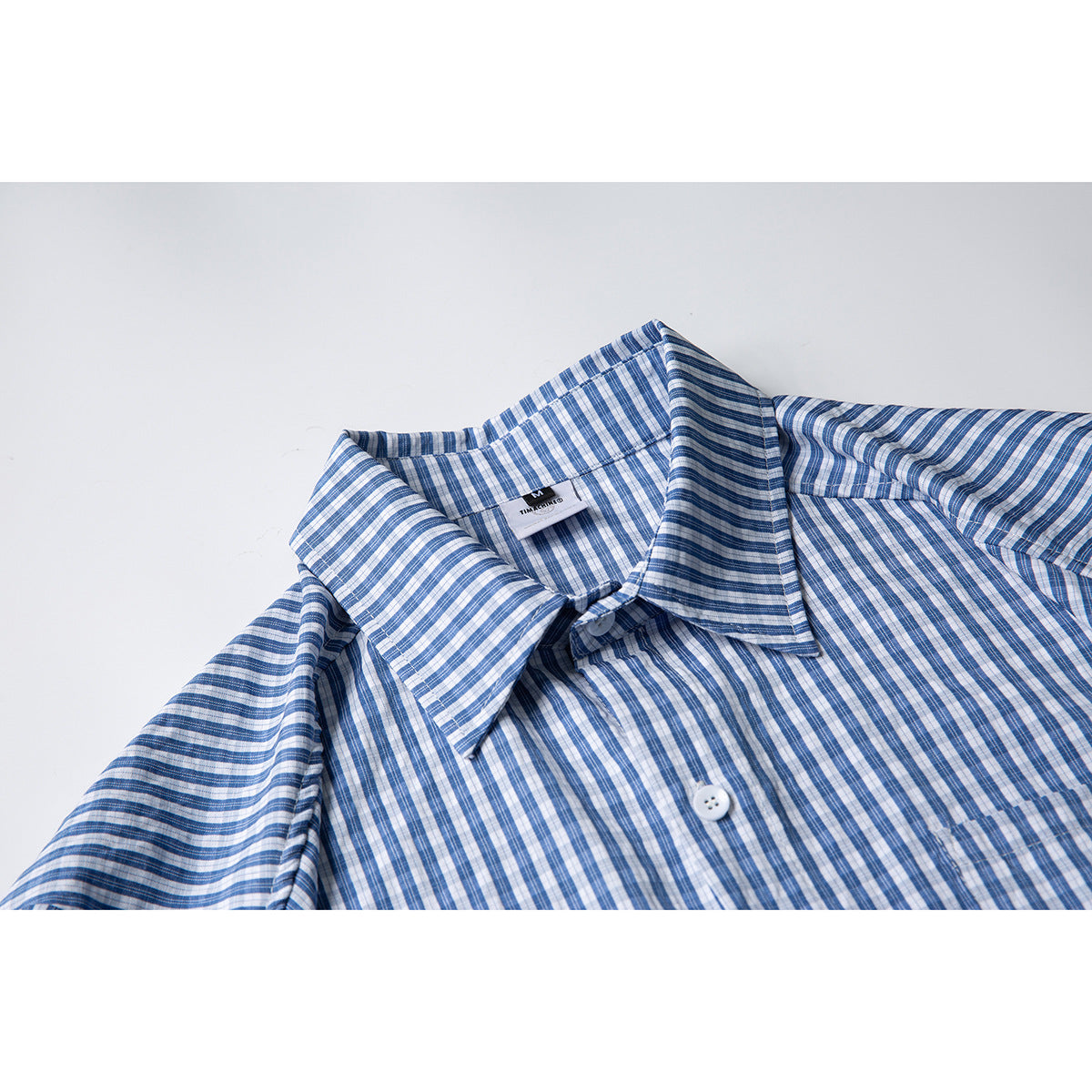 Close-up of a blue and white checked shirt collar, upper front, and white button.