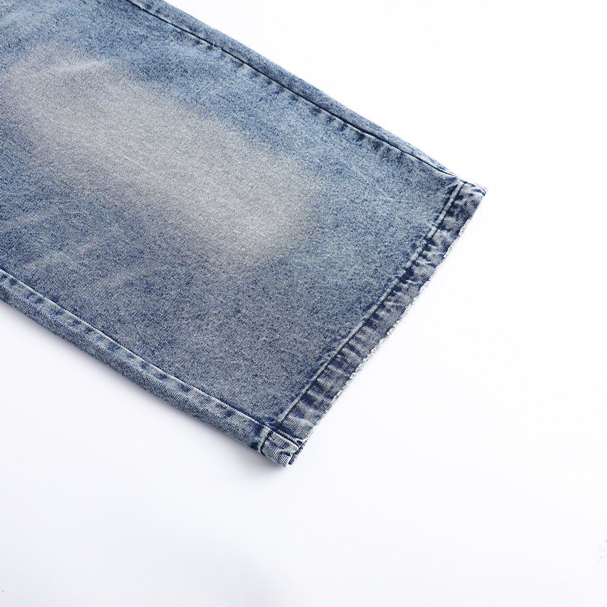 Close-up of the stitched hem on a blue acid-wash jeans leg.