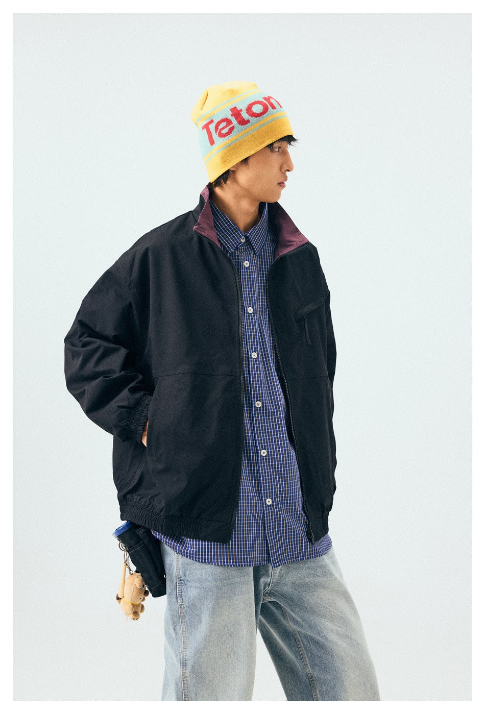 Model wearing a black zip-front windbreaker with a plum collar over a blue checked shirt.