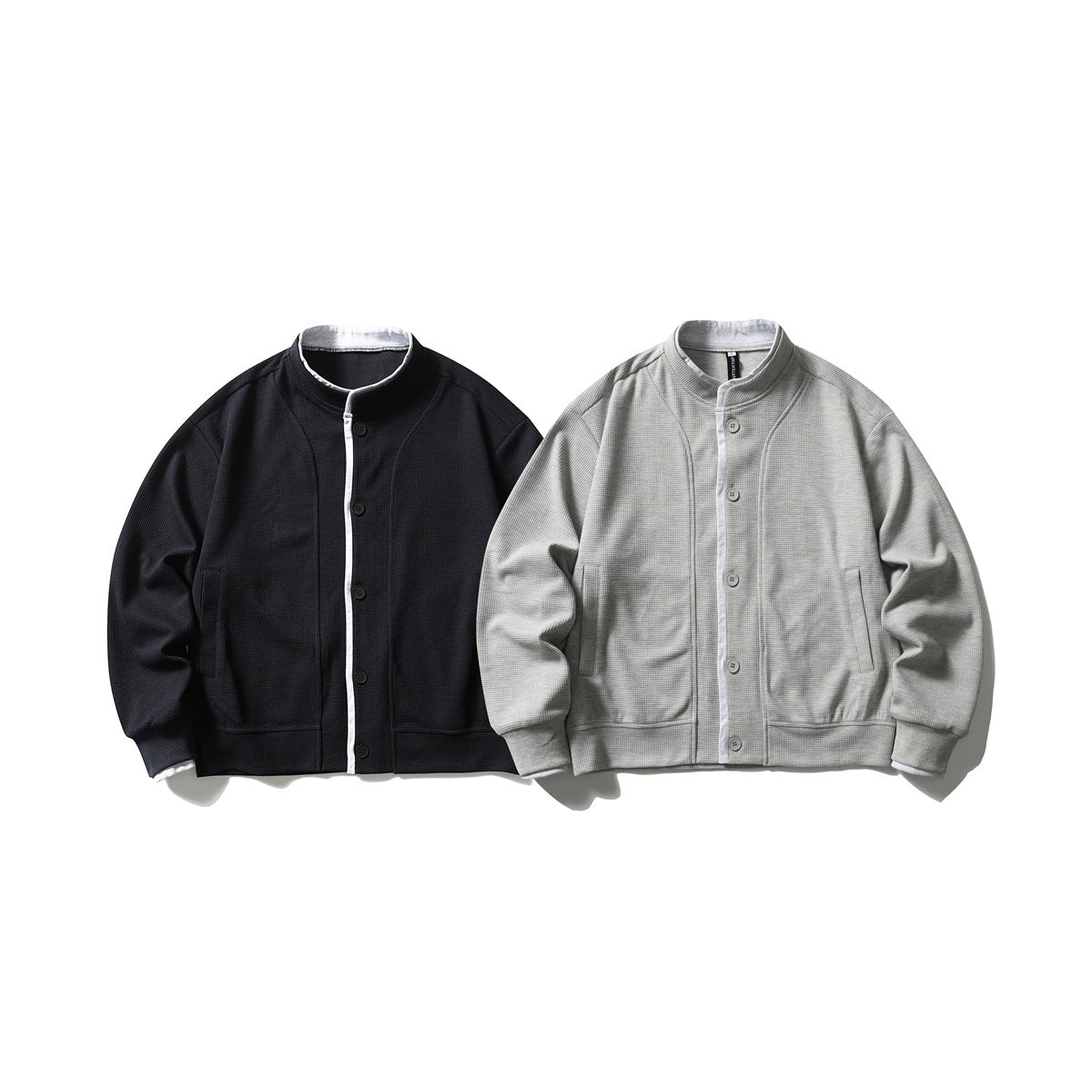 Two button-front jackets shown from the front: one black and one light gray, both with stand collars and pockets.