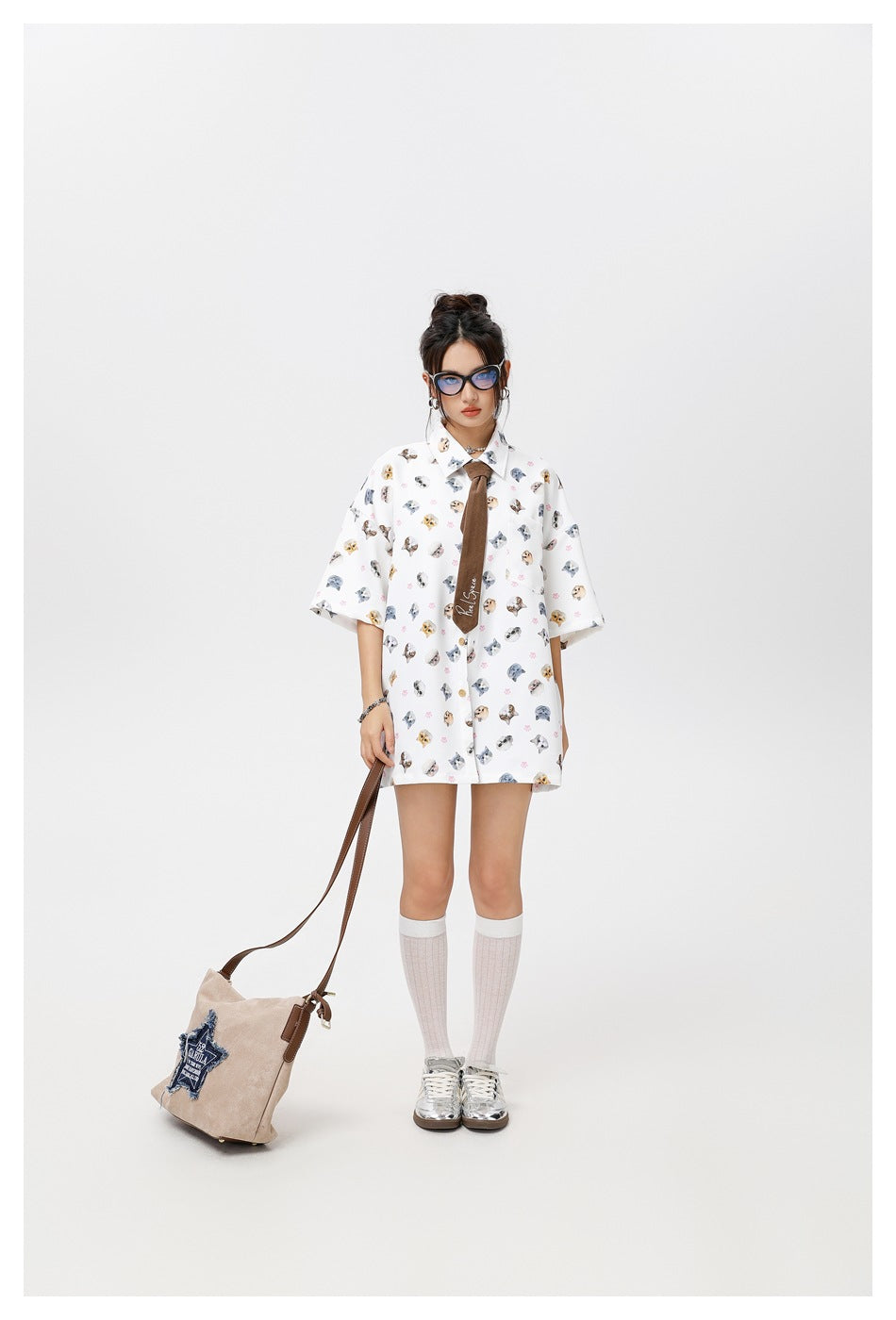 Full-length model wearing a white oversized cat-and-paw-print shirt with a brown tie and knee-high socks.