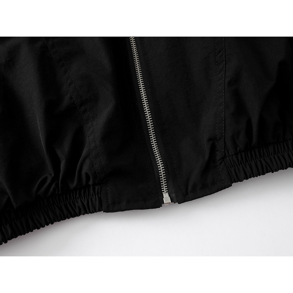 Close-up of a black jacket hem with an elasticated edge and silver zipper.