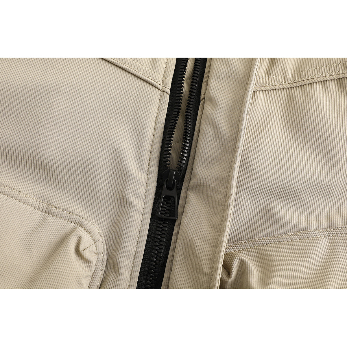 Close-up of the beige jacket's black front zipper, covered placket, and fine ribbed fabric.