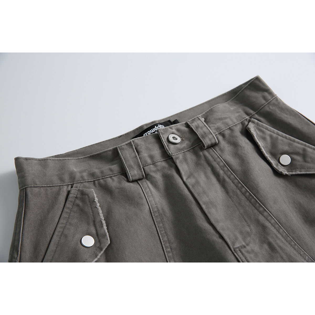 Close-up of gray shorts showing the waistband, belt loops, button, fly, and snap-button pocket flaps.