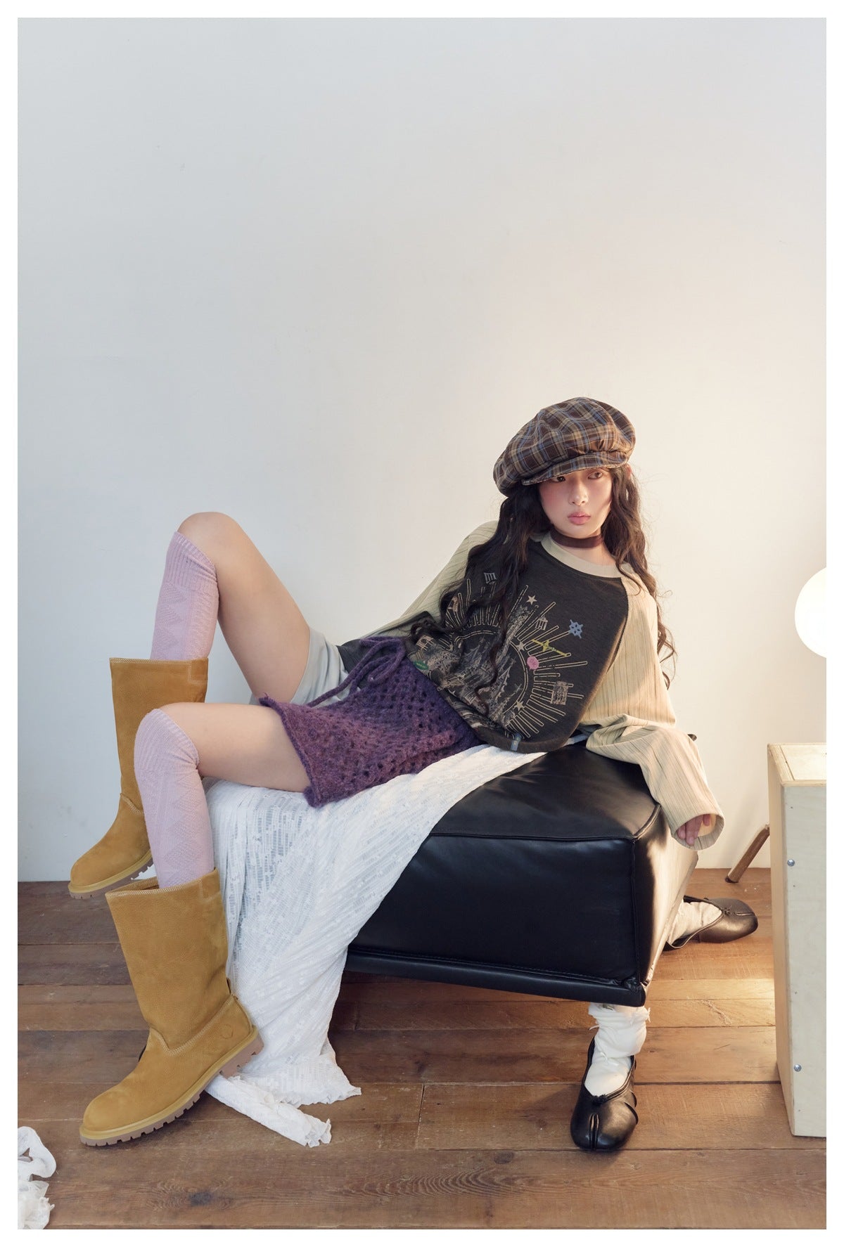 Seated model wearing a charcoal graphic raglan top with cream ribbed sleeves and a purple wrap skirt.